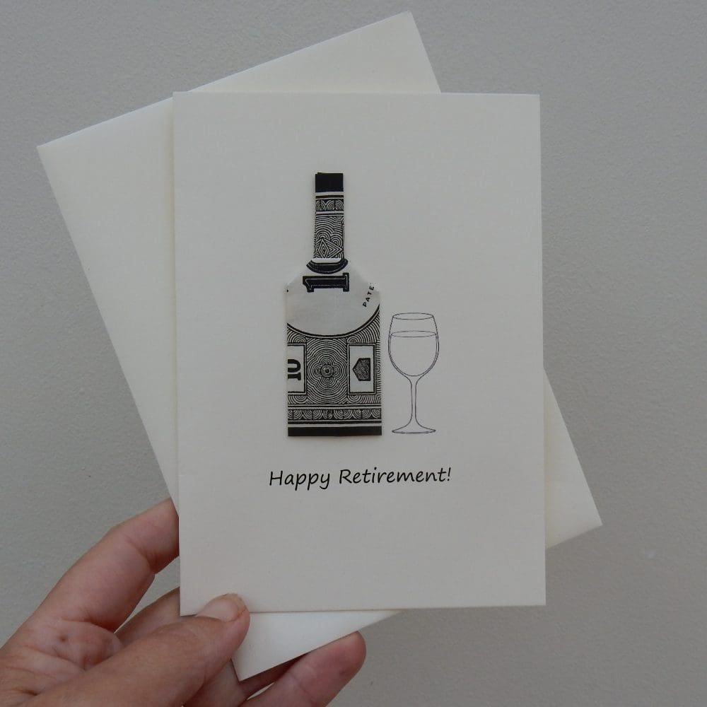Hand holding cream coloured Happy Retirement card. Origami folded bottle shape made using a sheet of monopoly money
