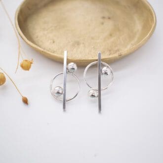 Silver earrings rest on brass dish on white background