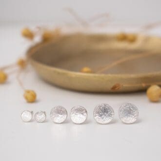Small round silver stud earrings all lined up on white background with small brass dish