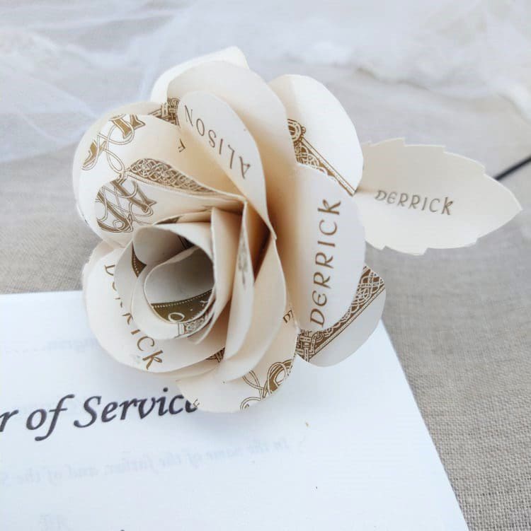 Single paper rose made using upcycled wedding stationery lying on an Order of Service