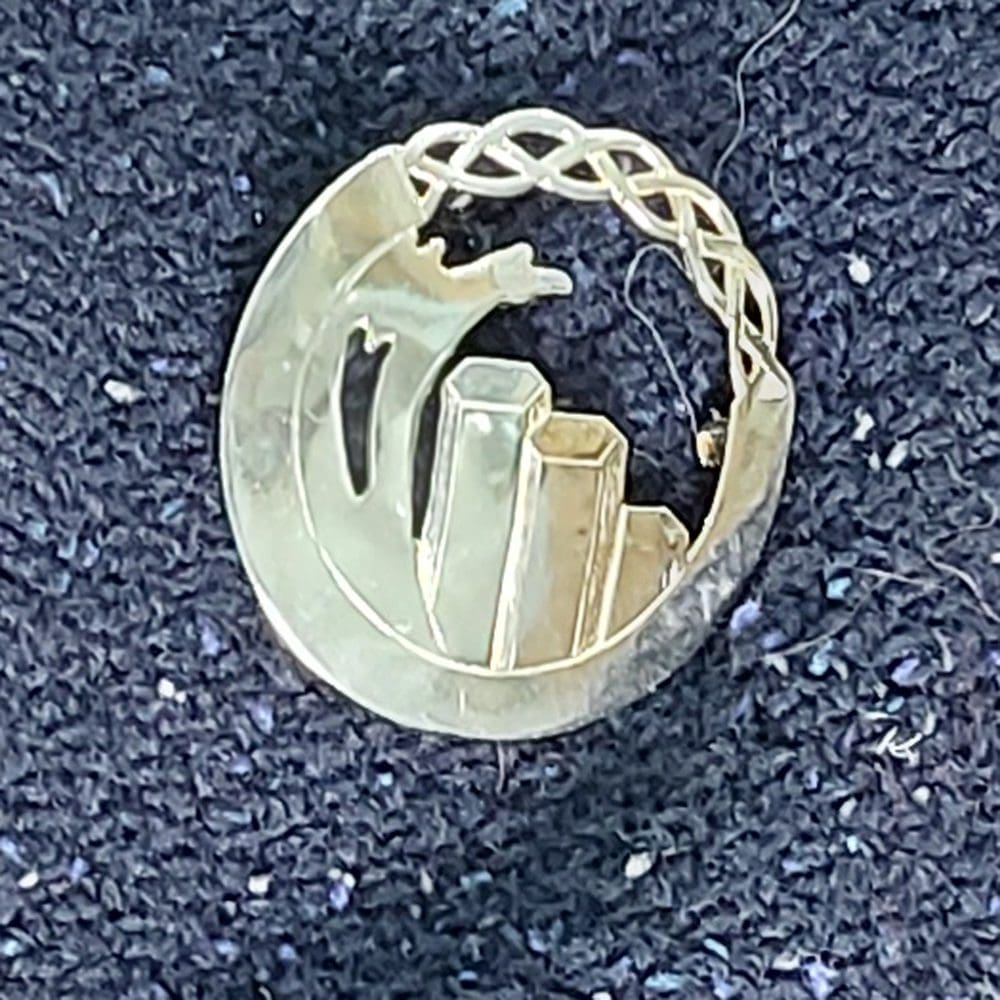 round brooch with Celtic design at the top right, a wave at the bottom left and Giant Causeway stones in the middle. The brooch is made of sterling silver.
