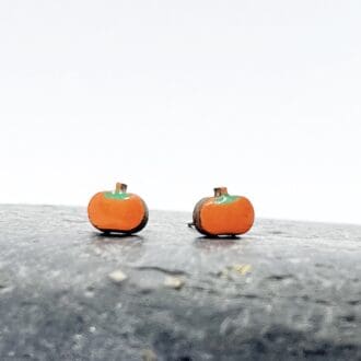 bright orange pumpkin earrings on a grey stone against a white background