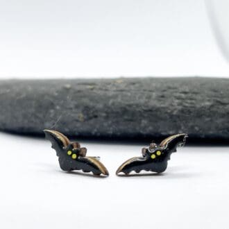 shiny black bat earrings with yellow eyes on front of a grey stone on a white background
