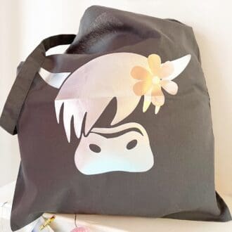 dark grey tote bag with a silver highland cow wearing a rose gold flower in her mane