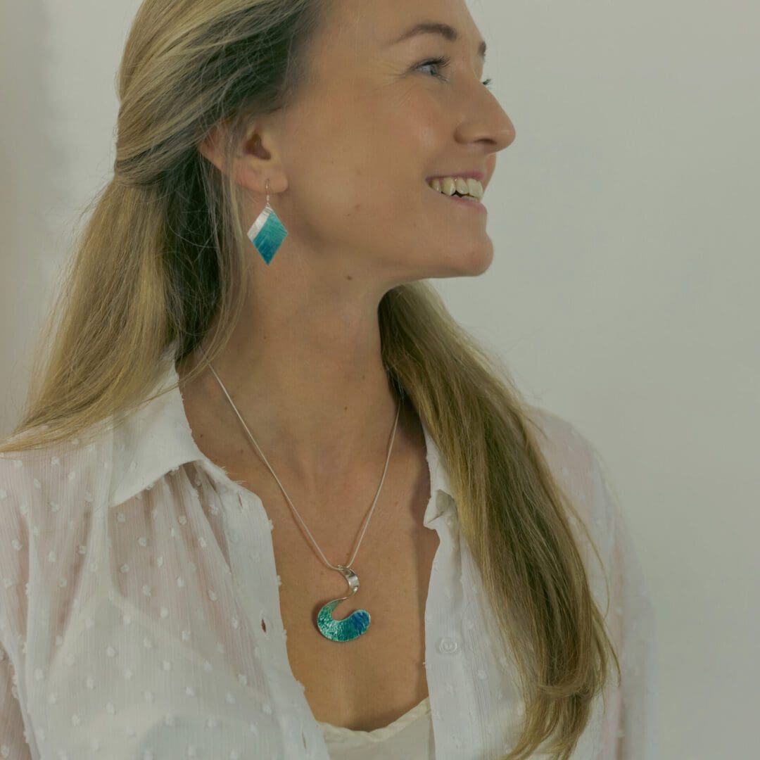 Girl wearing turquoise diamond shaped earrings with a matching enamelled pendant in the shape of a wave