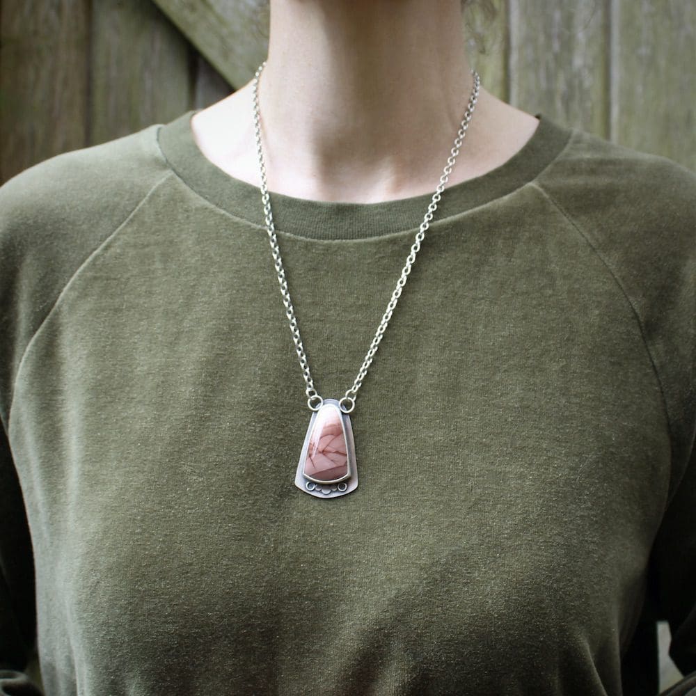 A sterling silver and pink imperial jasper statement pendant on a 22" chain, worn around the neck of a woman wearing a green velvet jumper.