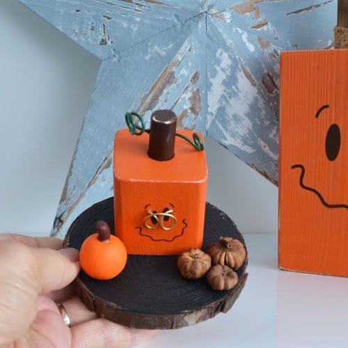 Fun Halloween or autumnal handmade wooden decoration with small square pumpkin wearing glasses and three mini dried pumpkins