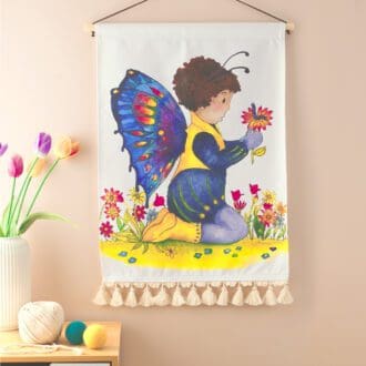 Cotton wall hanging featuring toddler dressed as a beautiful butterfly sat amongst the flowers interacting with his caterpillar friend Ideal for a child's nursery, bedroom or playroom