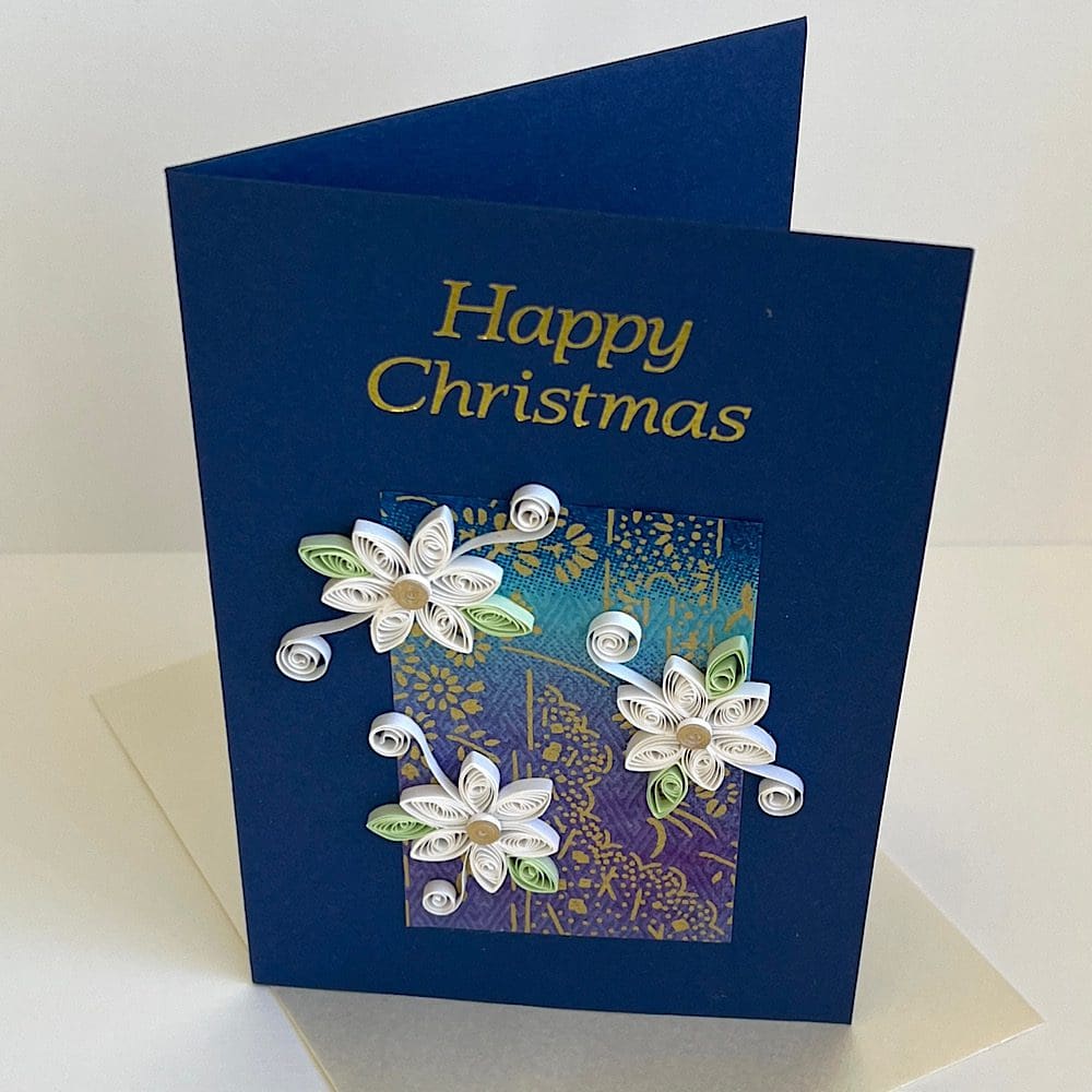 Handmade Christmas card with three quilled flowers on a navy blue base and Happy Christmas greeting in gold