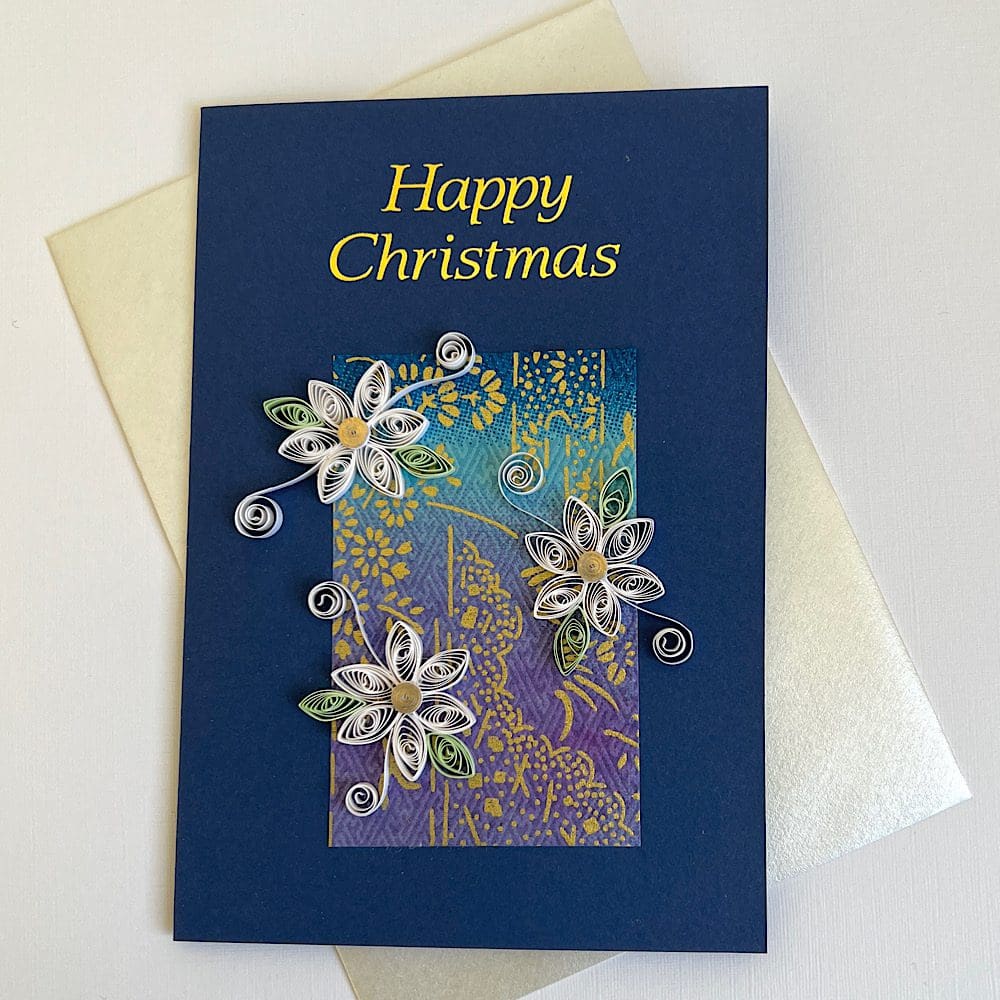 Handmade Christmas card with three quilled flowers on a navy blue base and Happy Christmas greeting in gold