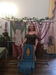 I am standing within my typical market stall with wallhangings behind me & holding a chair that is part of a pair I made as a commission. They have been shipped to America