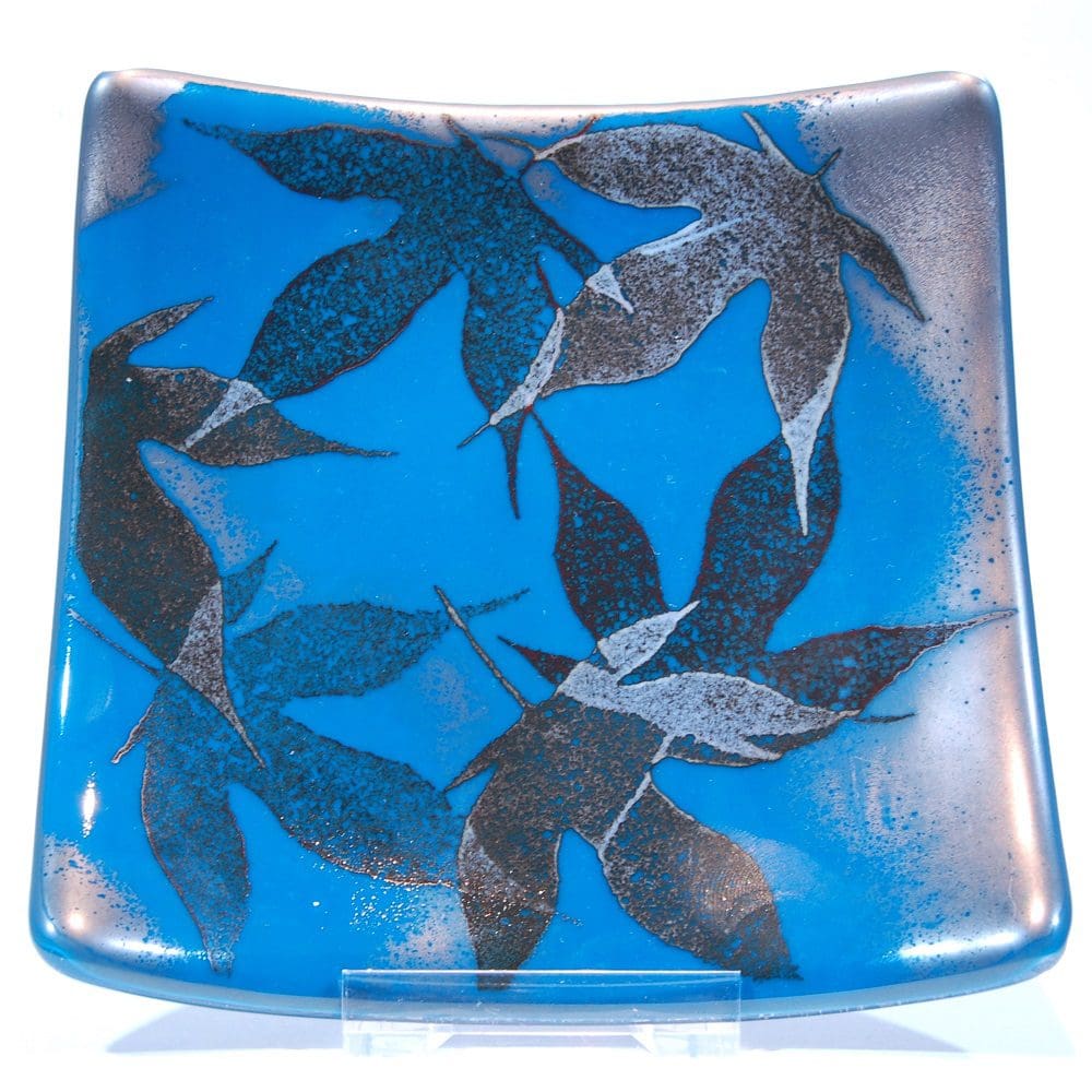 Front view of a teal blue square fused glass dish with a delicate pattern of maple leaves