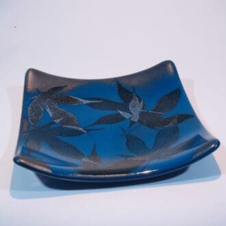 A teal blue square fused glass dish with a delicate pattern of maple leaves