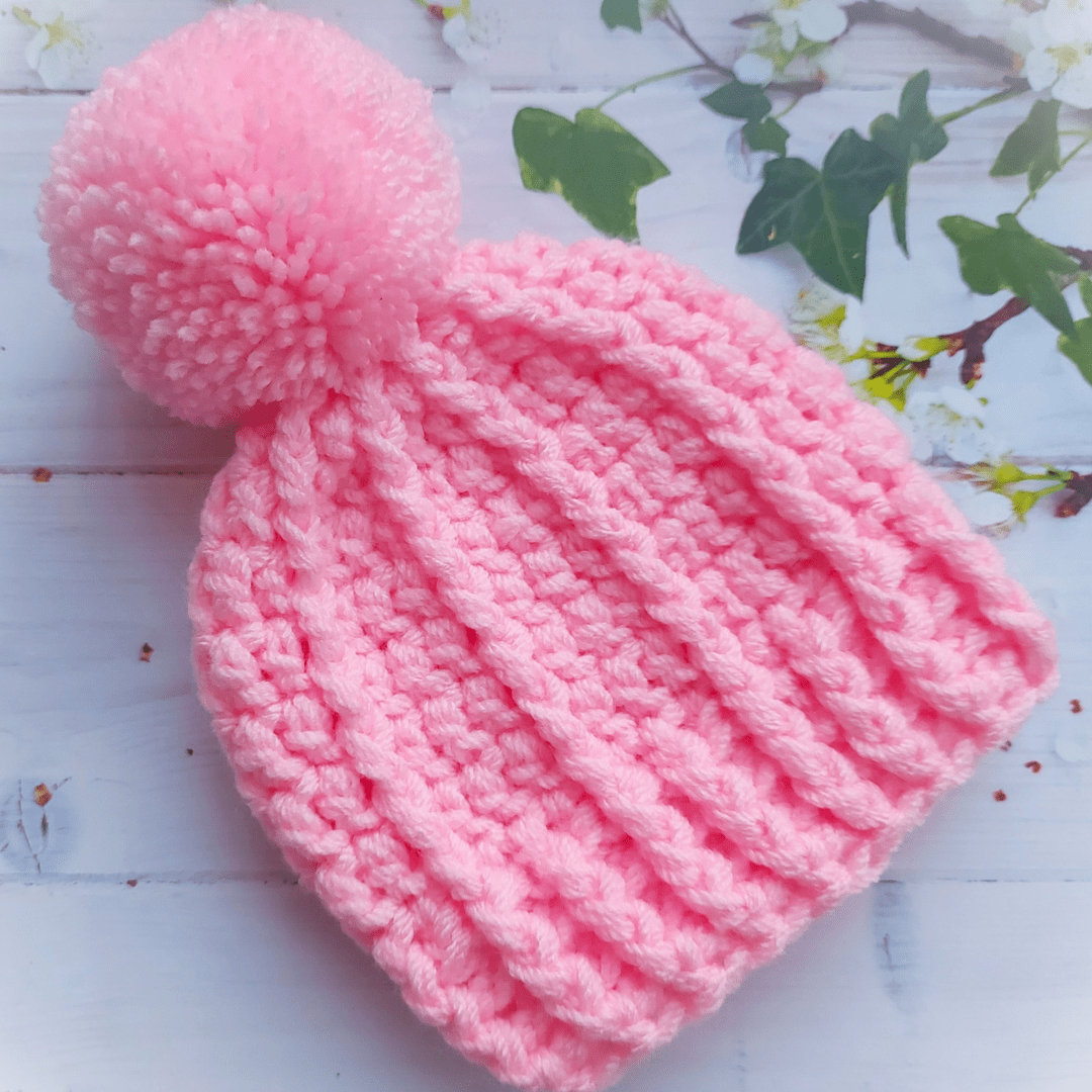 Pink Crochet Chunky Textured Pom Pom Bobble Hat In Size 0-3 months, made with 2 strand of arylic yarn creating texture and warmth. Handmade yarm pom pom attached.