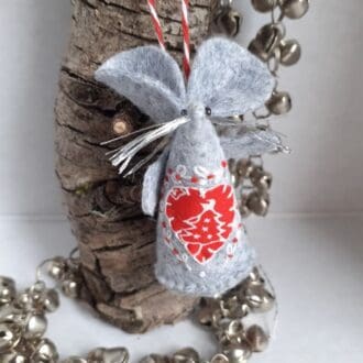 a handmade felt mouse christmas decoration, with a fabric heart with a scandi design surrounded by embroidery.