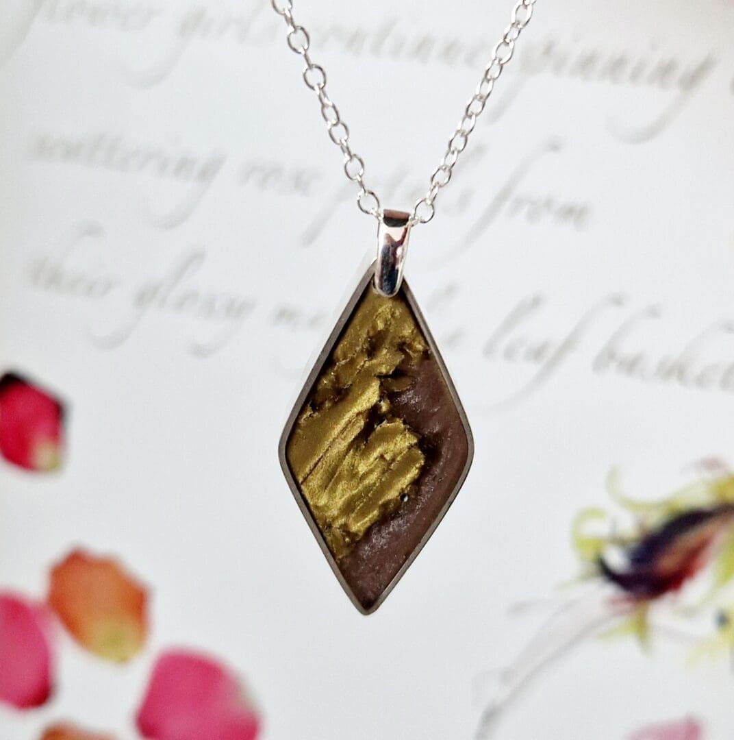 Sterling silver pendant with a diamond shape frame filled with gold toned clay and dusky pink pearlescent resin on a sterling silver trace chain