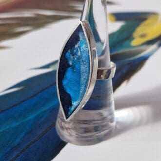 Sterling silver statement ring with an elongated leaf shape frame filled with clay and resin in tones of ocean blue on a hammered band