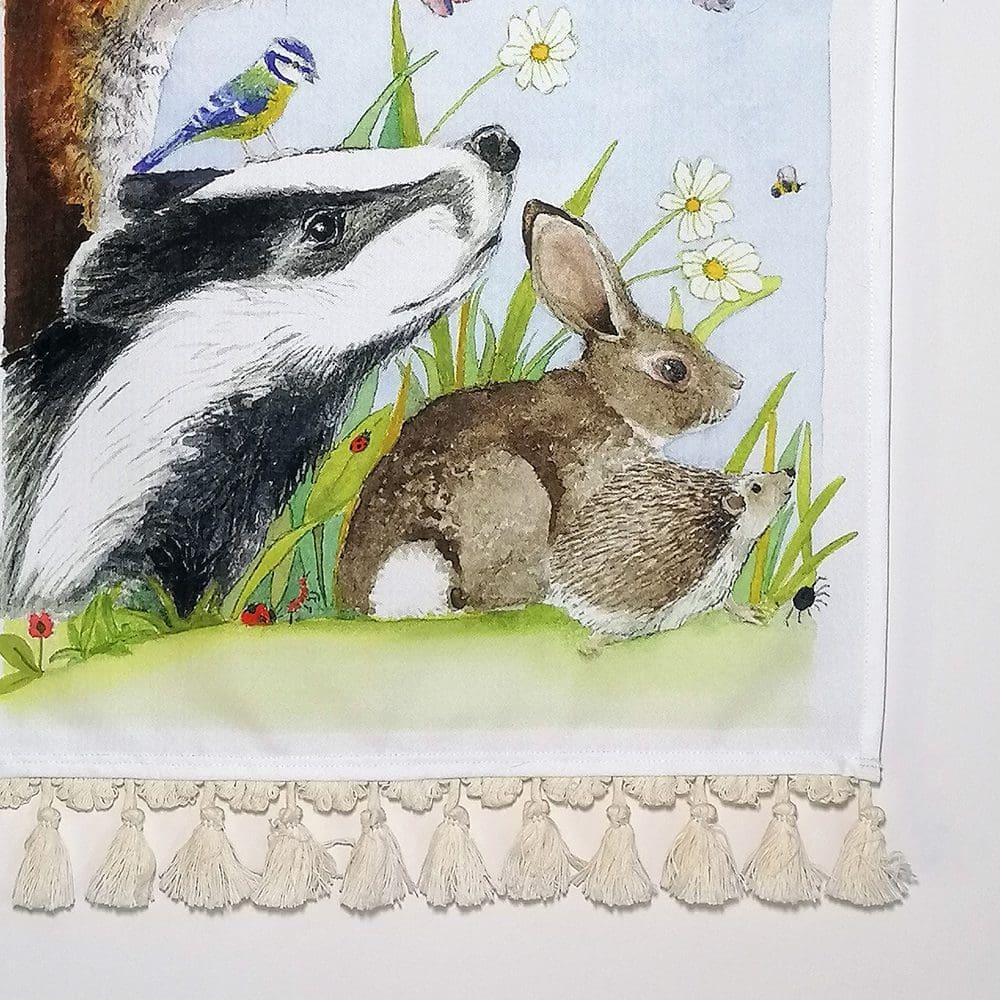 Close up detail of the British wildlife friends wall hanging - heavy weight cotton fabric showing the badger, rabbit and hedgehog and the pale cream cotton tassel decoration. Original illustration created as a watercolour painting.