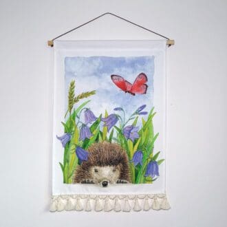 Brown hedgehog hiding amongst the blue harebells and long grasses visited by a pink butterfly friend. Printed on heavyweight cotton, the wall hanging has a wooden pole hanger, fine brown leather hanging chord, and a decorative cotton tassel border giving a contemporary look to the lovely wall decor.