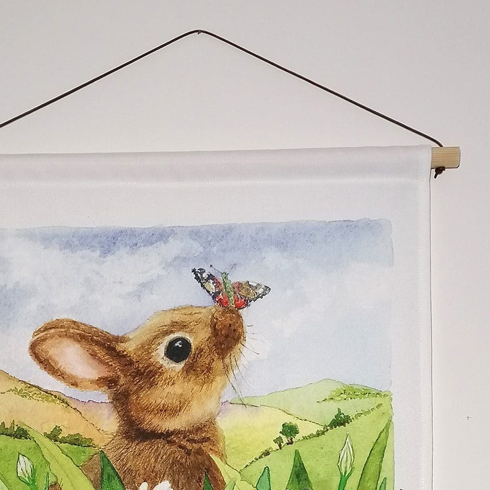 Close up detail of the rabbit and butterfly wall hanging - wooden pole hanger and waxed cotton chord. Original illustration created as a watercolour painting.