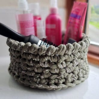 A green floral patterned crochet storage basket holding bathroom accessories