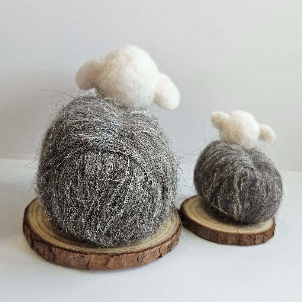 Back view of small and large needle felted herwick sheep on wood slice