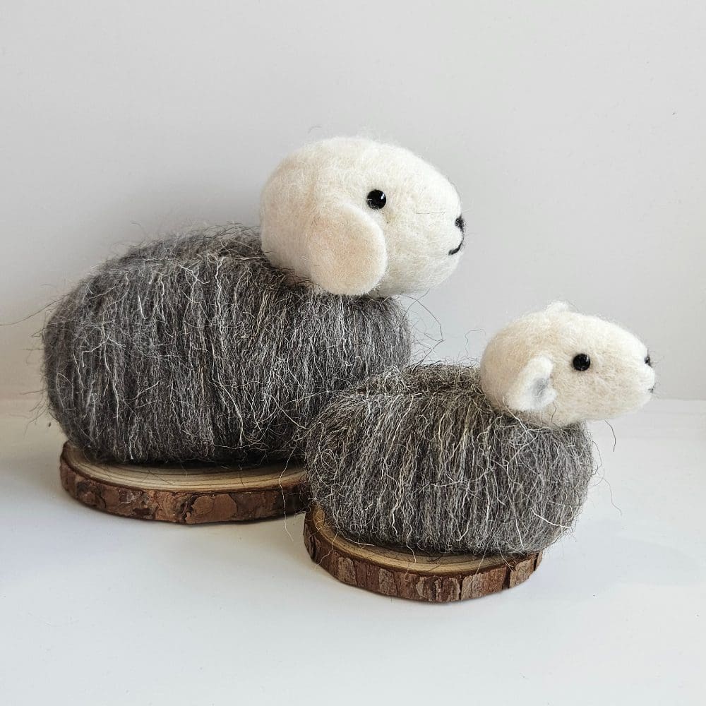 Side view of small and large needle felted herwick sheep on wood slice