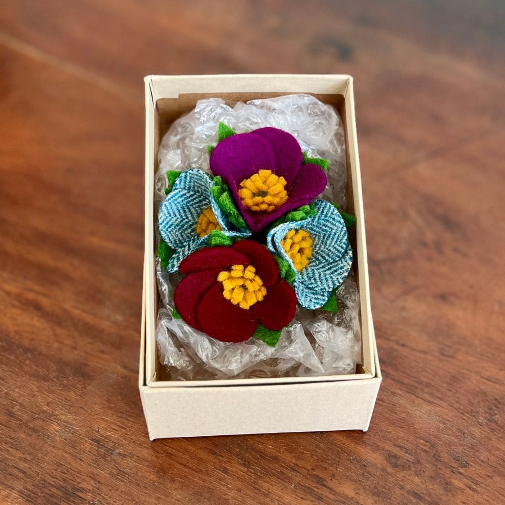 Photo shows a four flower 1940s style brooch in a brown box. the blooms are supported by bubble wrap ready for posting.