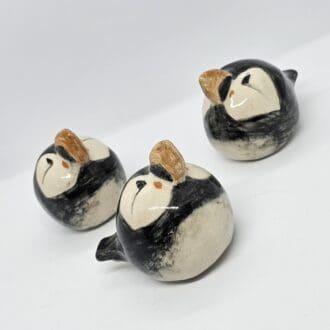 On a white background, 3 ceramic puffins face in different directions, beaks proudly to the sky