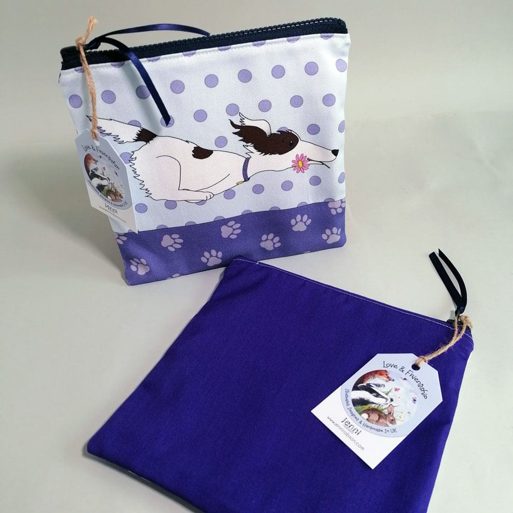 Flat, cotton toiletries bag featuring a zooming dog with a pink flower in its mouth. Various shades of purple and pale blue, spotty background, paw print base and a dark purple back.
