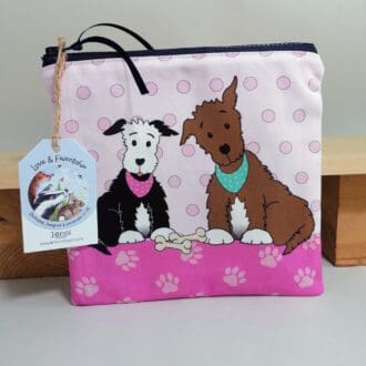 Flat, cotton toiletries bag featuring two dogs in bandanas with their bones. Various shades of pink spotty background, paw print base and a pale pink back.