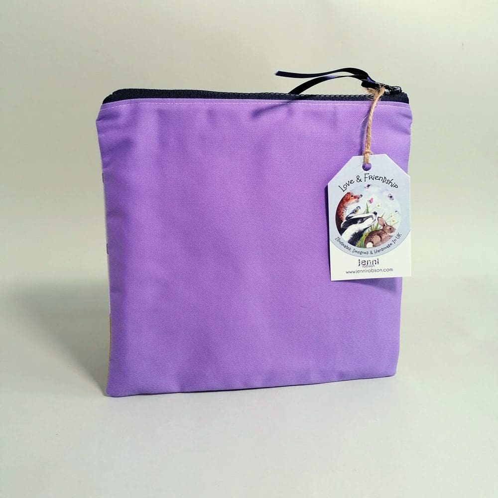 Flat, cotton medium toiletries bag featuring a sweet little dog in his best bandana. Various shades of purple spotty background, green paw print base and a pale purple back.