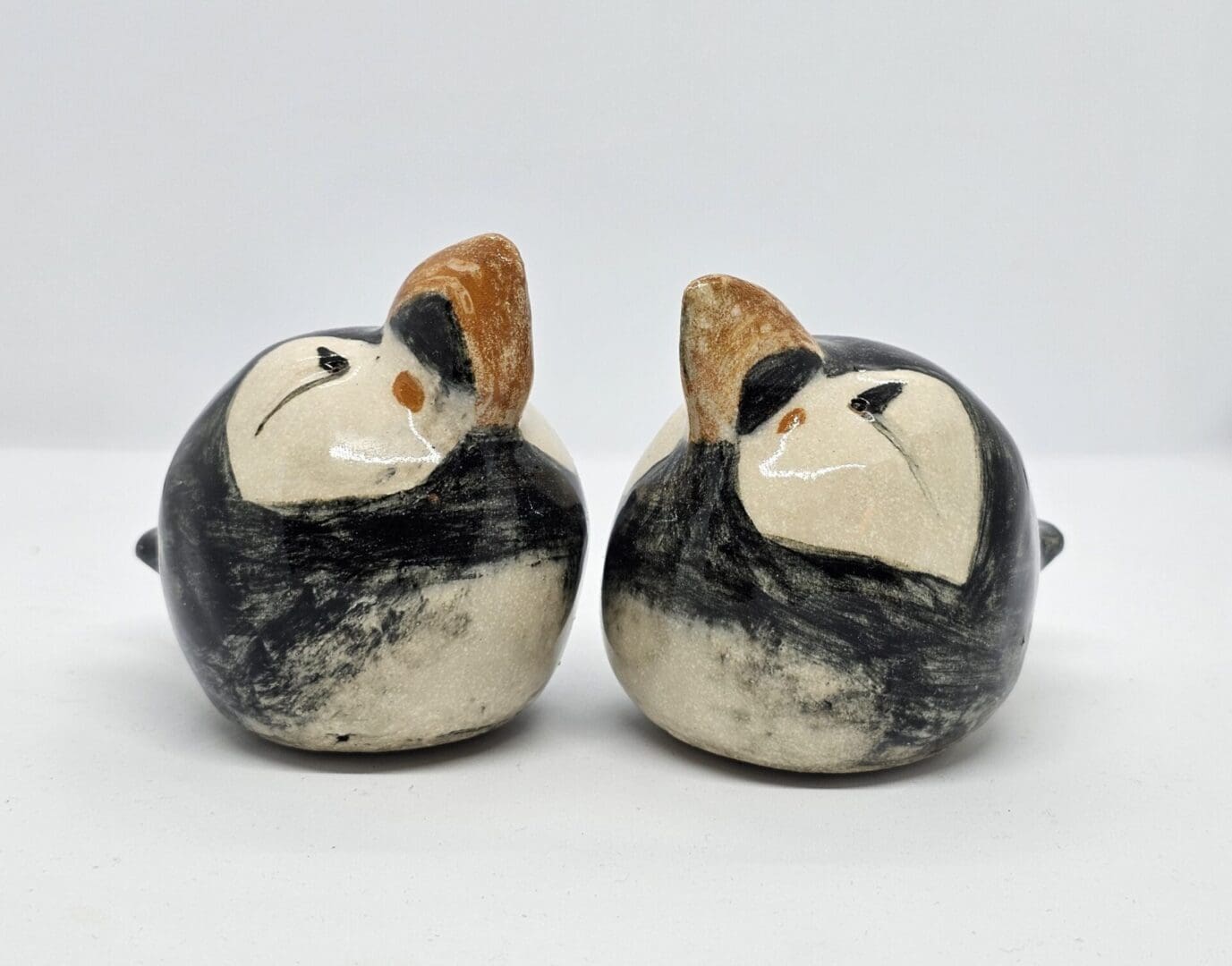 On a white background, 2 ceramic puffins sit nose to nose