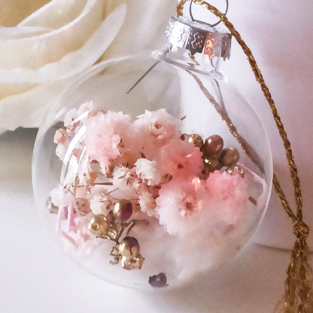 Glass Christmas decoration with natural pink, white and gold encased in the glass bauble with a gold thread loop, rests on a white background.