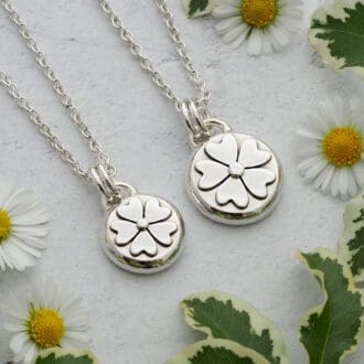 Two round argentium sterling silver pebble pendants featuring a flower with five heart-shaped petals.