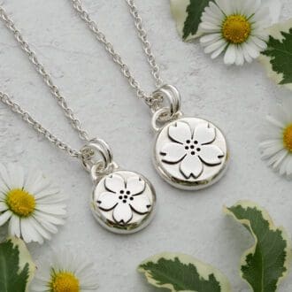 Two round argentium sterling silver pebble pendants featuring a cherry or apple blossom flower with five petals.
