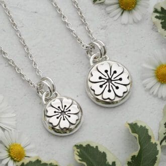 Two round argentium sterling silver pebble pendants featuring a folk art style flower with 7 petals.