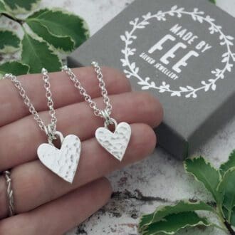 Handmade sterling silver hammered heart pendants in two different sizes on belcher chains shown on hand with Made By Fee branded jewellery box