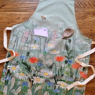 Wildflower cotton apron with adjustable neck fastening and pocket. Printed with illustrations of poppies, daisies and a friendly bee.