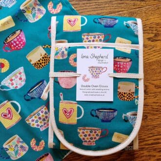 Teal coloured oven gloves with towelling reverse, printed with illustrations of colourful tea cups and biscuits.