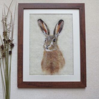 A handmade needle felted picture of a brown hare on a cream wool background in a dark wood effect frame.