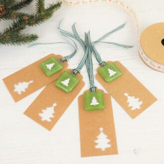 Four Kraft gift tags each with a handmade fused glass and paper cut Christmas tree keepsake