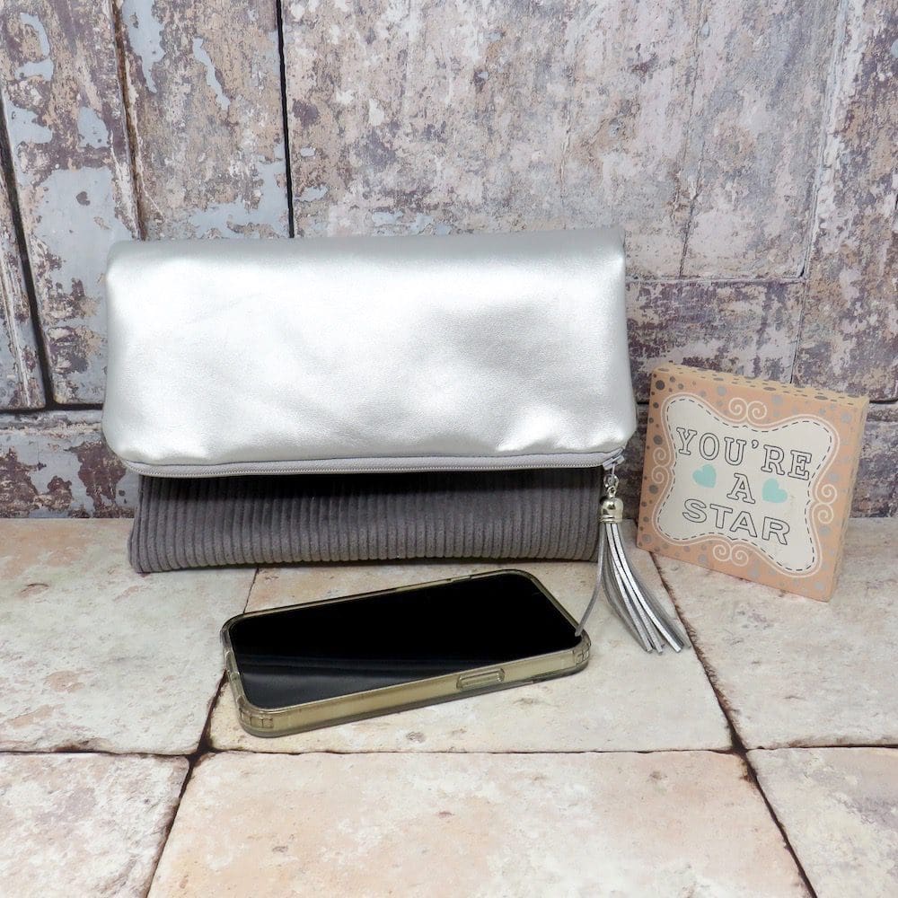 A reversible fold over zip top clutch in a silver faux leather and a grey jumbo cord.
