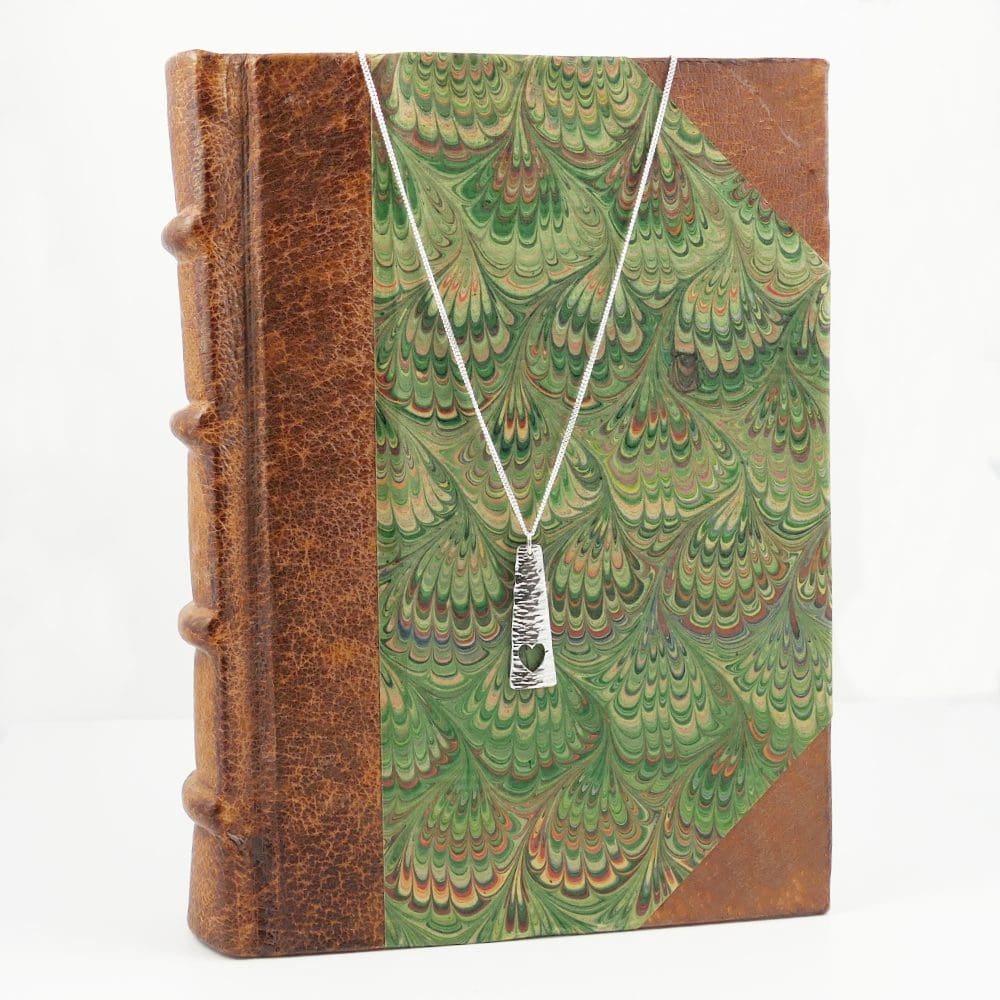Silver-triangle-bar-heart-pendant-and-chain-hanging-on-a-book-cover