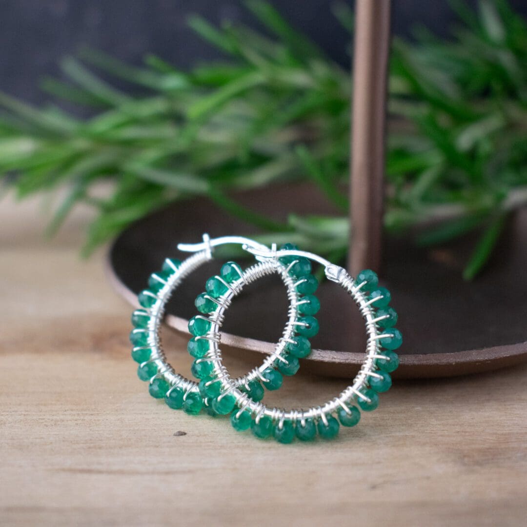 green beaded hoop earrings resting on brass dish with foliage in background