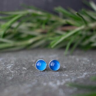 blue onyx gemstone stud earrings resting on slate with rosemary foliage in background
