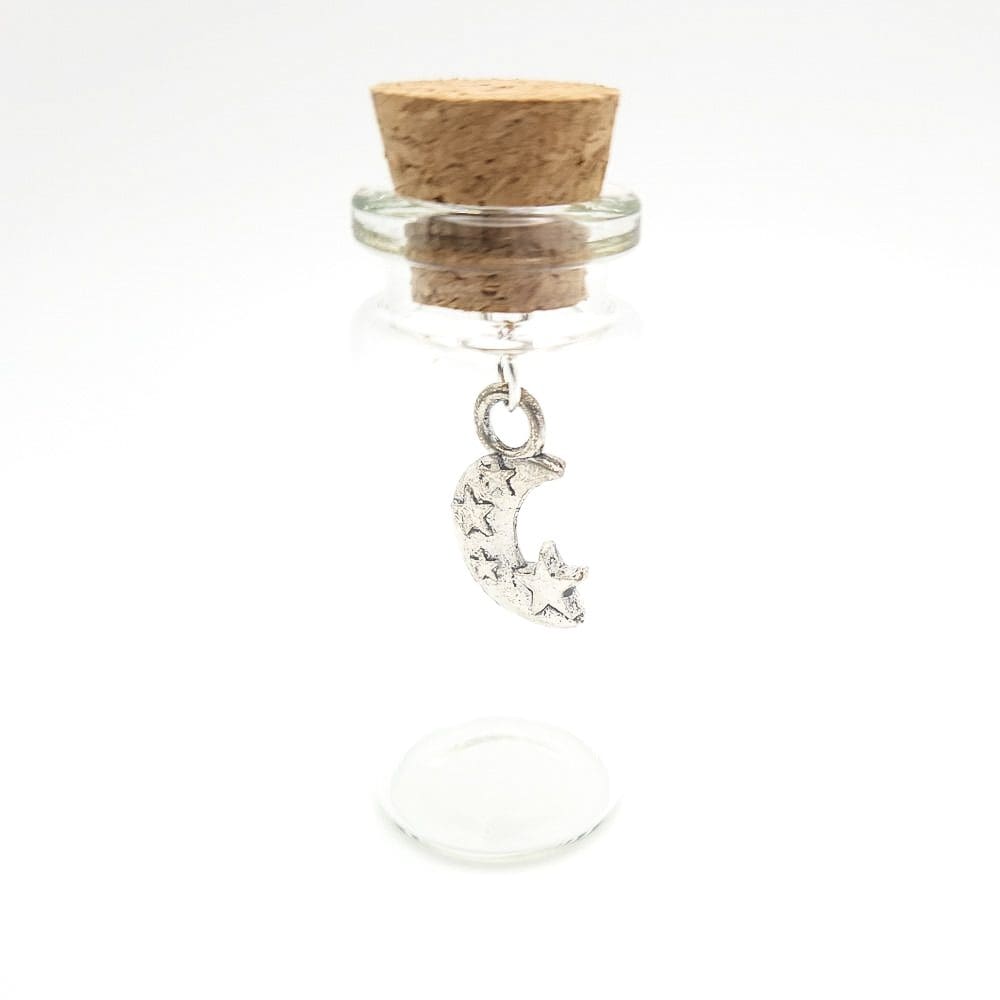 A small glass bottle with a silver moon and stars charm inside it by under the blossom tree