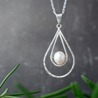 teardrop shaped silver wire necklace with pearl centre hung over black background