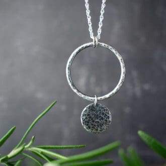 silver circles necklace over black background with rosemary leaves in foreground