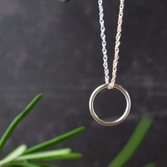 silver ring hung on sterling silver chain over black background with rosemary leaves in foreground